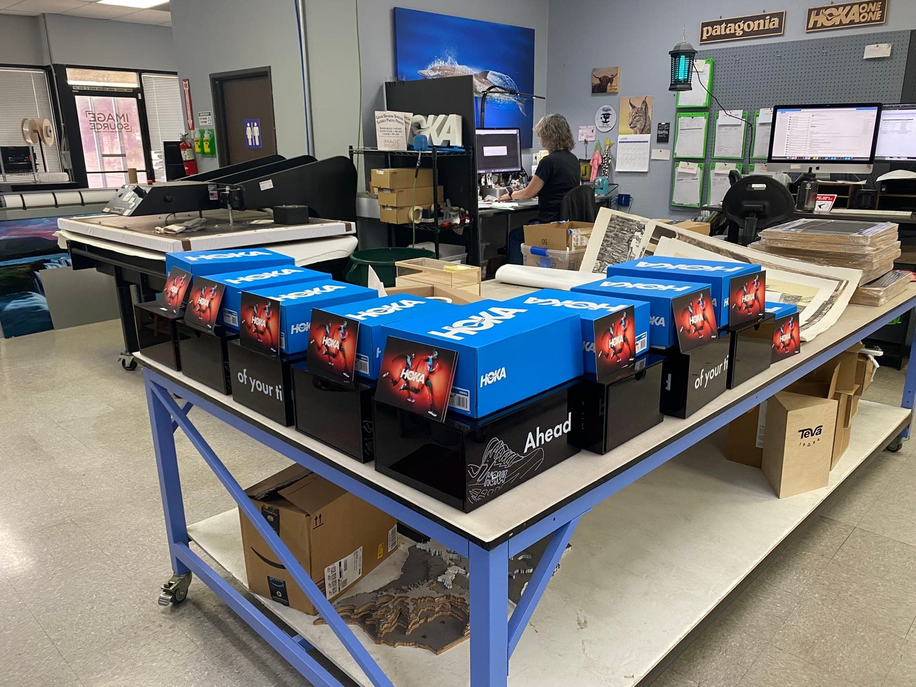 Image Source production floor — HOKA shipping displays staged on a workbench, Patagonia and HOKA wood signs on the wall, flatbed printer in the background.